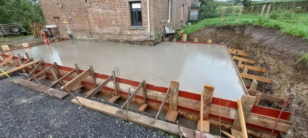 Dalle de béton coulée dans un coffrage en bois, en bas d'un bâtiment en briques