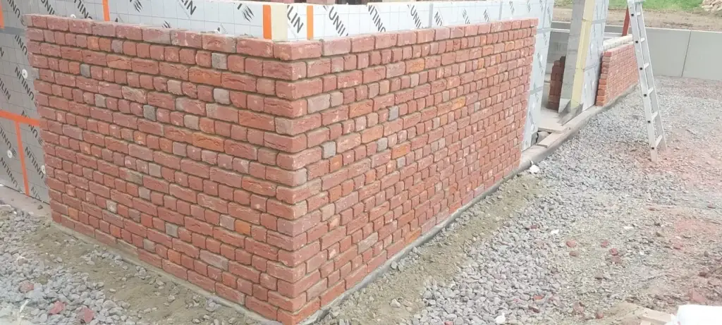 Mur en briques rouges monté devant un isolant, au pied du chantier