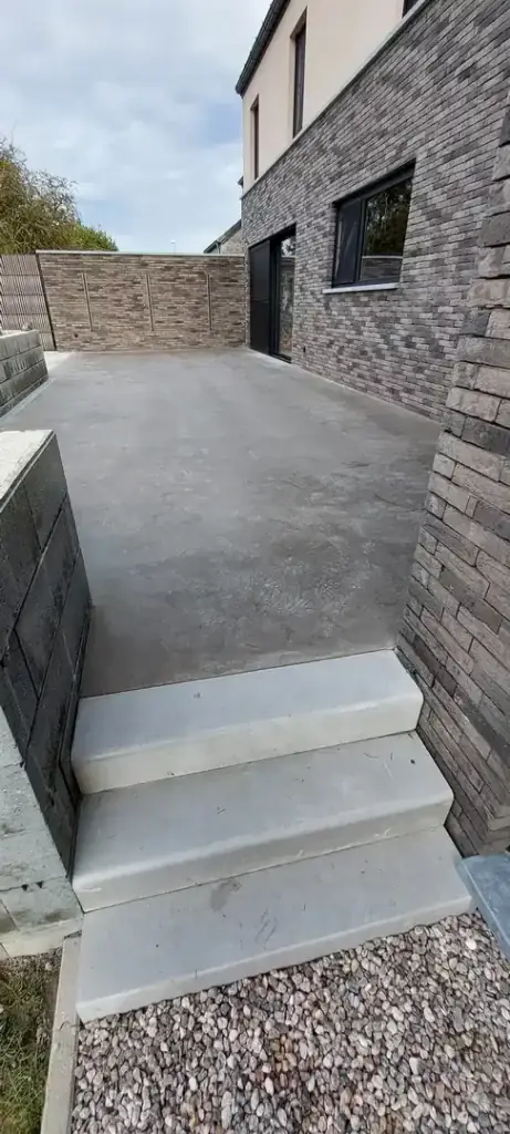 Terrasse en béton lissé avec marches, le long d'une façade en briques grises
