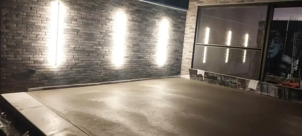 Mur de briques sombres éclairé par des appliques, sol en béton lissé